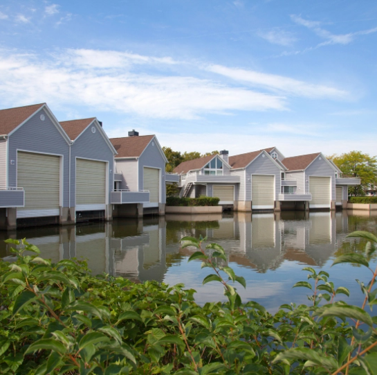 A series of houses by the water, featuring a pond in the background.